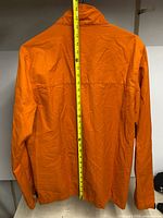 Back view of orange Nike jacket with measuring tape indicating length