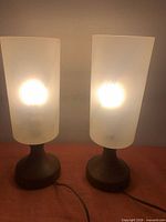 Both lamps illuminated showing frosted shades and teak bases