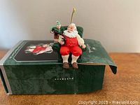 Ornament displayed on box showing Santa in chair with Coke bottle and elf