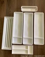 Overview of six white organizer trays laid out on wood floor