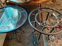 Two metal round tables showing overall style, glass present on one, missing on other