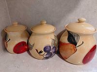 Front view of three ceramic fruit canisters with lids