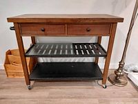 Front view of wood and metal rolling cart showing drawers, shelves, casters