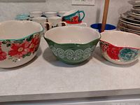 Three mixing bowls with floral and lace designs, mugs visible in background