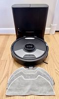Robot vacuum docked in black self-empty base with gray mop pad displayed in front
