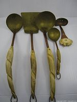 Front view of five copper and brass utensils showing handles and heads