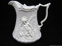 Full left profile of white parian jug showing relief cherub, handle and spout