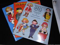 Three Dolly Dingle paper doll books fanned out showing front covers