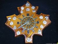Front view of maple leaf-shaped wood wall clock with ship-wheel dial and Canadian military badges