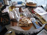 Overall view of supplies on tabletop including partial hull, plans, wood, tools