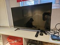 Front view of Insignia 32" TV on stand with two remotes and Bell box visible