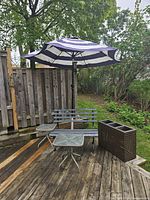 Complete outdoor set on deck showing bench, umbrella on stand, planter and two tables