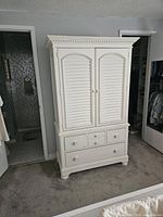 Front view of white solid wood armoire showing louvered doors and six drawers