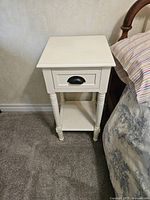 Full view of white painted side table beside bed