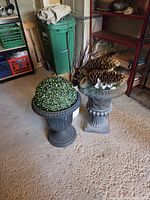 Two urn planters with topiary and pine-cone arrangement on garage floor