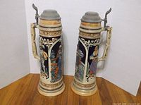 Front view of both lidded steins showing relief scenes and pewter lids