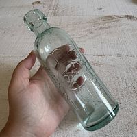 Bottle held in hand showing embossing and Codd neck