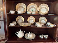 Full view of three cabinet shelves showing Wedgwood dinnerware, Royal Albert teapot and additional small pieces