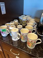 Group of seventeen mugs on countertop showing variety of patterns and quantities
