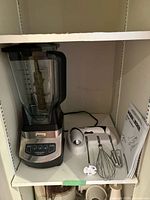 Ninja blender, Black & Decker mixer with accessories and manual on shelf