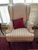 Front view of wing back chair showing upholstery, pillow, wooden legs