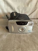 Front view of Canon Sure Shot 65 Zoom camera showing lens, flash, branding and case behind