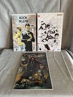 Three bagged and boarded comics laid out: Book of Death, DC variant, Lady Mechanika