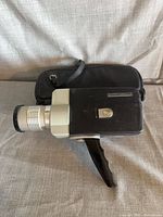 Side view of Hanimex Synchro Zoom movie camera with attached zoom lens and folded pistol grip alongside black zippered case