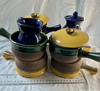 Four handled casserole bowls stacked, two yellow lids, sugar and creamer visible