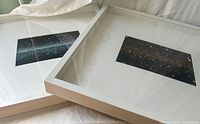 Two framed prints side by side on bed showing frame depth and matting