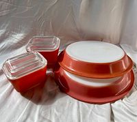 Two red refrigerator dishes with lids alongside two pie plates, one red and one flamingo pink