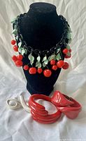 Group shot of necklace, two red bracelets and white brooch