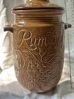 Front view of brown stoneware Rumtopf jar with lid showing fruit motifs and script