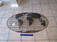 Full view of oval metal world map on tiled floor with 12-in ruler for scale
