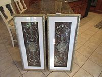 Full view of both framed metal wall panels standing side by side on tile floor