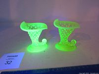 Two uranium glass hobnail cornucopia vases glowing under UV light