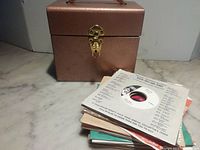 Stack of records beside bronze metal carrying case