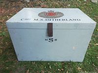 Front view of painted wood foot locker showing lid crest, name and latch