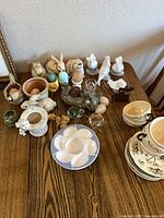Overview of table with ceramic and glass items including egg plate, soup bowls, planters, figurines