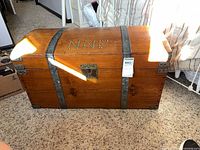 Front view of wooden dome-top steamer trunk showing latch, bands, monogram, overall size