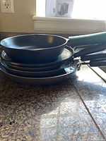 Stack showing three Farberware nonstick pans with silver rims and one cast iron skillet on top