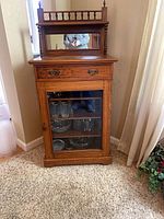 Front view of oak curio cabinet showing drawer, glass door, mirrored back and spindle gallery