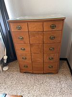 Front view of five-drawer wood chest, brass pulls visible, glass top in place