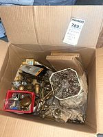 Open box containing assorted brass knobs, lamp parts, red tray of small hardware, octagonal container of screws