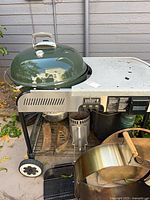 Overview of Weber Performer grill with green lid closed on cart, chimney starter, charcoal baskets, pizza oven ring visible