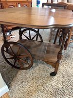 Side view of wooden bar cart showing wheels, turned legs and lower shelf