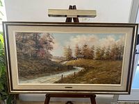 Full view of framed painting on easel with attached picture light