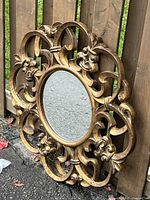 Full view of ornate gilt round mirror leaning against wooden fence