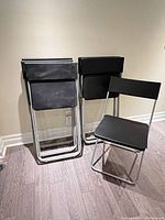 Six black plastic folding chairs, five folded one open