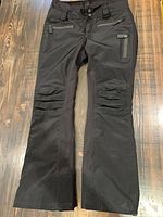 Full view of black SOS ski pants front showing pockets and knees